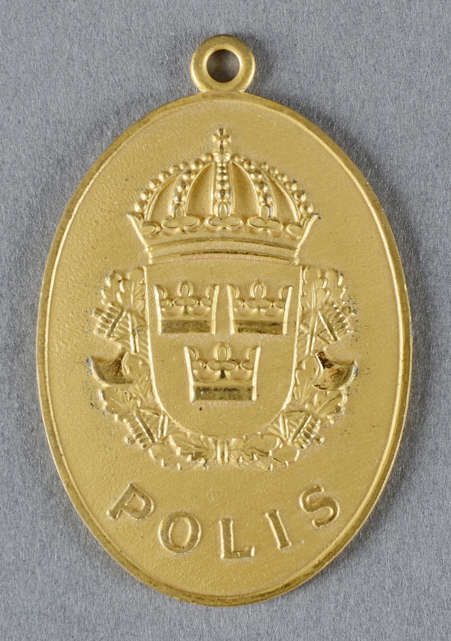 Goldene Medaille mit einer Kroneförmigen Polizeimarke in der Mitte, mit eingravierter Schrift.