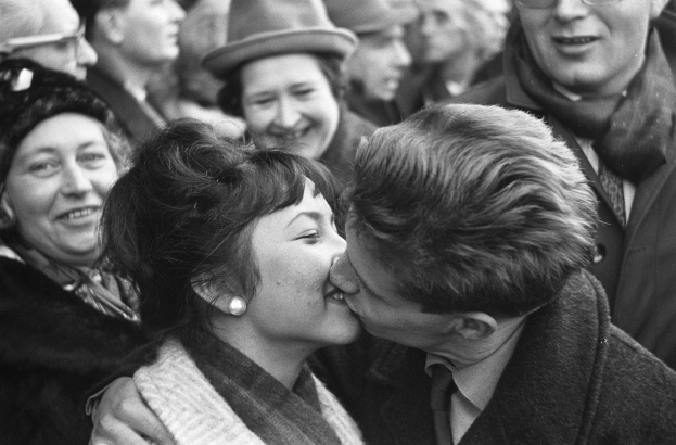 Ein Schwarz-Weiß-Foto eines Mannes und einer Frau, die leidenschaftlich vor einer lachenden Menge küssen.