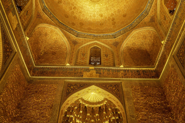 Innenraum einer iranischen Moschee mit detaillierten Wanddesigns, einem Fenster im Hintergrund und einem eleganten Kronleuchter an der Decke.