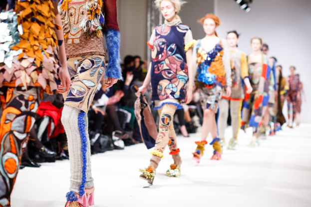 Eine Gruppe von Frauen, die auf dem Laufsteg der London Fashion Week gehen, mit unscharfen Zuschauern und heller Beleuchtung, die einen traumhaften Effekt erzeugen.