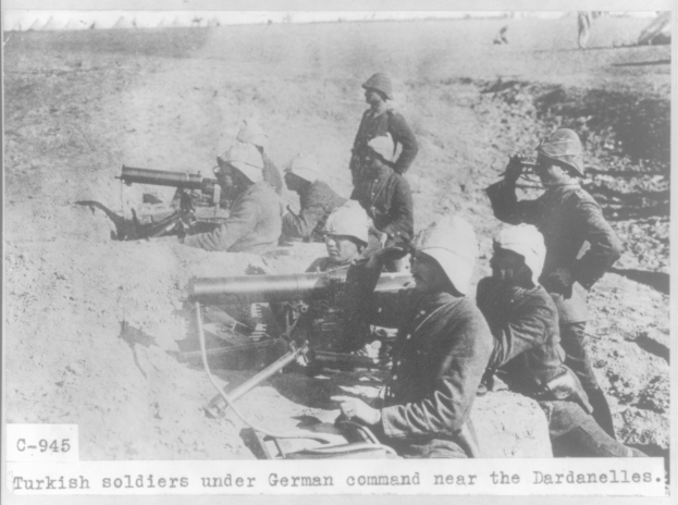 Schwarzes und weißes Foto einer Gruppe von türkischen Soldaten unter deutschem Kommando in der Nähe der Dardanellen, die Helme tragen und Waffen halten, mit Text unten.