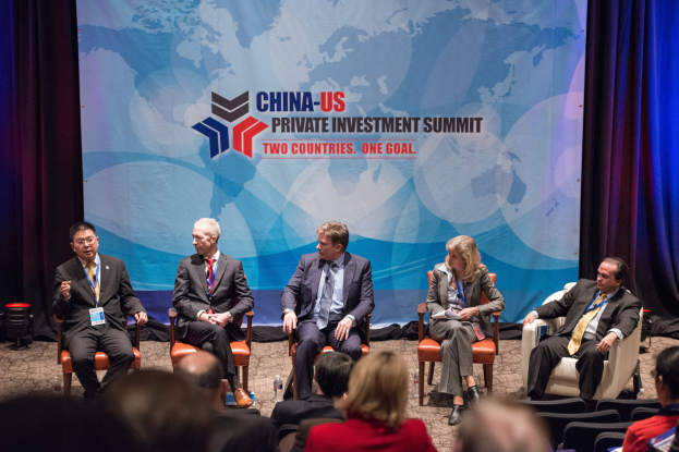 Eine Gruppe von Menschen, die auf Stühlen sitzen und einem Bildschirm mit Text und einer Karte gegenübersitzen, mit Vorhängen im Hintergrund, was auf einen China-US-Privatinvestment-Gipfel hindeutet.