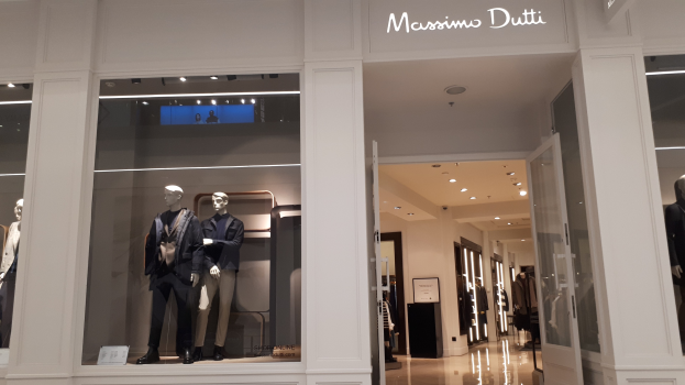 Vitrine von Massimo Dutti in Mailand, Italien, mit Schaufensterpuppen in moderner Kleidung, beleuchteter Decke, Informationsschildern und sichtbarem Boden.