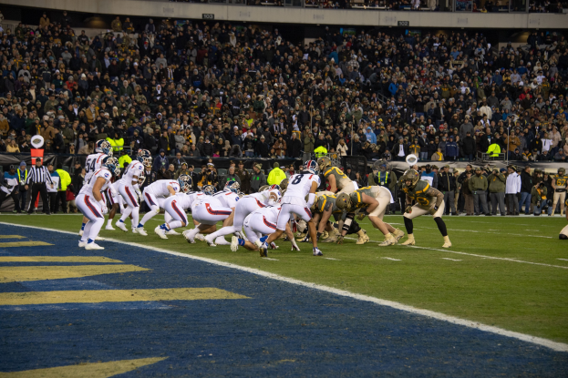 Amerikanische Football-Spieler in rot-weißer Uniform und Helm auf dem Feld liegend während eines Spiels in einem Stadion mit Zuschauern und Werbetafeln im Hintergrund.