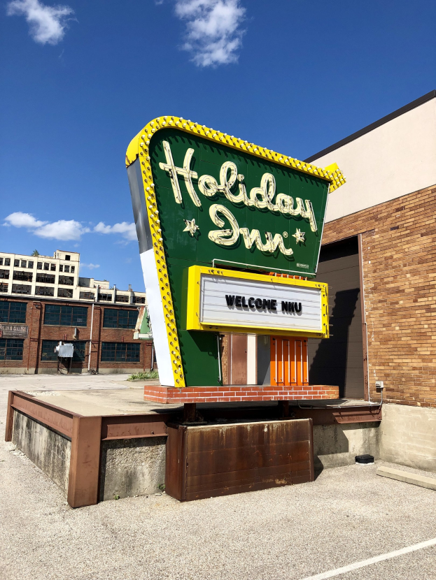 Holiday Inn Schilder an einem Gebäude mit einem Textboard davor, bewölkter Himmel, Fenster im Gebäude sichtbar.