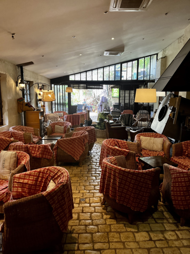 Ein geräumiges Hotelfoyer mit zahlreichen Stühlen, Tischen, gepolsterten Sofas, wandmontierten Lampen, Deckenklimaanlage und Glasfenstern an der Rückseite.