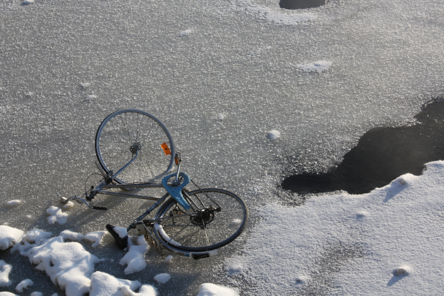 Ein Fahrrad liegt im Schnee neben einer Pfütze Wasser und ist von einer Schneedecke umgeben.