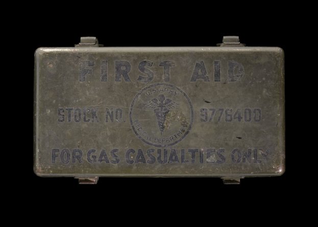 Metallischer Verbandkasten mit der Aufschrift "Verbandkasten für Gasopfer" vor schwarzem Hintergrund.