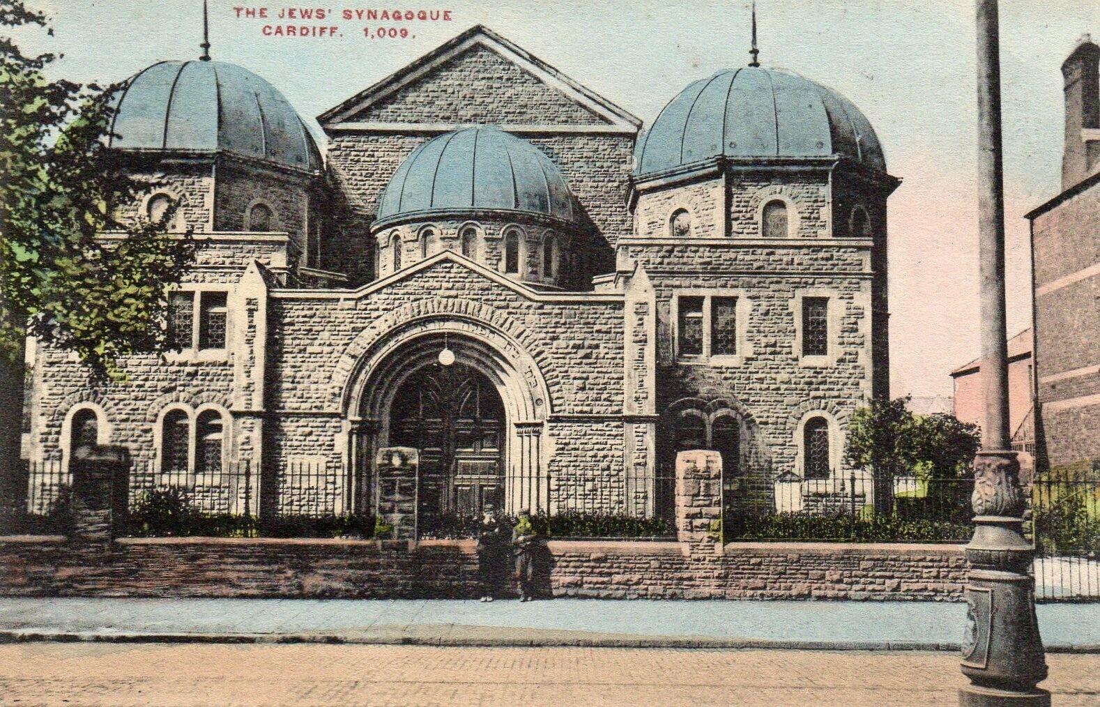 Alte Ansichtskarte der jüdischen Synagoge in Cardiff, Ontario, Kanada, die ein Gebäude mit Fenstern, Türen und Bögen zeigt, umgeben von Pflanzen, einem Zaun, Bäumen, einem Pfahl und einem bewölkten Himmel, mit Text oben.