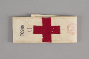 Ein rotes Kreuz-Ersthelfer-Set in einem Stoffbeutel mit Text und einem Stempel, das auf einer Oberfläche liegt.