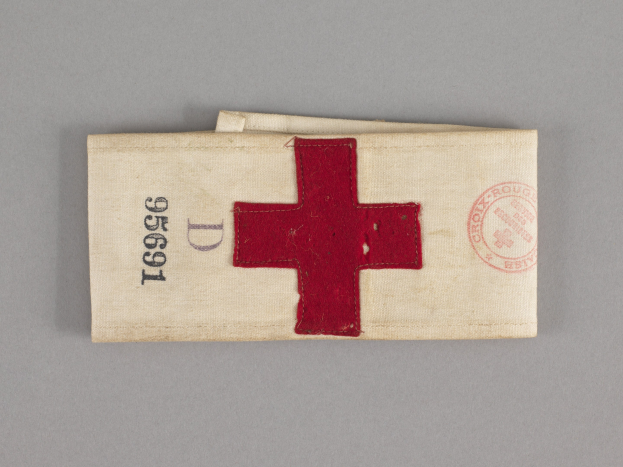 Ein rotes Kreuz-Ersthelfer-Set in einem Stoffbeutel mit Text und einem Stempel, das auf einer Oberfläche liegt.