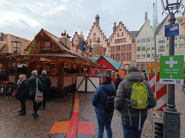 Menschen auf einem Kopfsteinpflasterweg neben einem Weihnachtsmarkt in Nürnberg, Deutschland, mit Laternen und Texttafeln in der Nähe, Gebäude im Hintergrund und einem bewölktem Himmel.