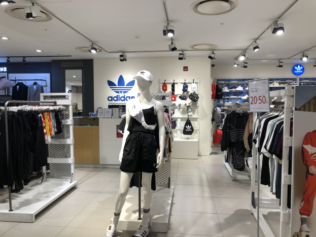 Innenansicht eines adidas Retail-Stores in Singapur mit Schaufensterpuppen, Kleiderständern, einer Texttafel auf der rechten Seite und Deckenbeleuchtung.