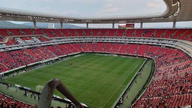 Großes Stadion voller Zuschauer bei einem Fußballspiel, mit Hügeln und einem klaren blauen Himmel im Hintergrund.