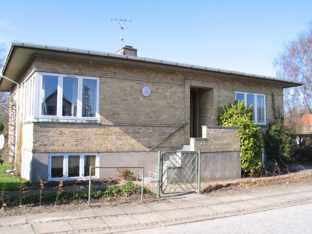 Außenansicht eines frei stehenden Bungalows mit zwei Schlafzimmern zum Verkauf in St. Johns Wood, Swindon, mit Dach, Fenstern, Tür, Treppe, Metallzaun, Pflanzen, Gras, Bäumen, Satellitenschößantenne und bewölktem Himmel.