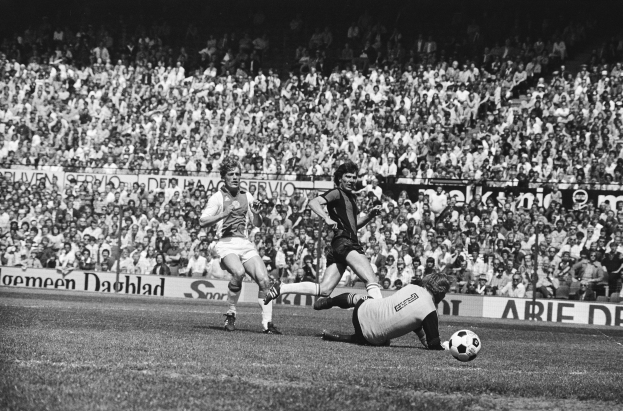 Schwarz-weißes Foto von Männern, die auf einem Feld Fussball spielen, mit Zuschauern im Hintergrund und einerBanner mit der Aufschrift "Bundesliga 1978-79 Ajax 1-1 Hannover 96".