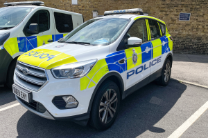 Zwei Polizeiwagen nebeneinander auf einem Parkplatz geparkt, mit einer Wand und einer Tafel im Hintergrund.