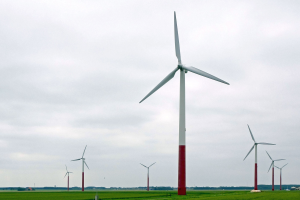 Eine Gruppe hoher, weißer Windkraftanlagen in einem grünen Feld mit Bäumen und Wolken im Hintergrund.