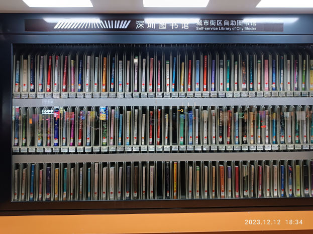 Eine gut beleuchtete Bibliothek mit hohen Bücherregalen voller Bücher, mit einer Texttafel und einem Wasserzeichen unten, die an eine Selbstbedienungsbibliothek der Stadtblocks erinnert.