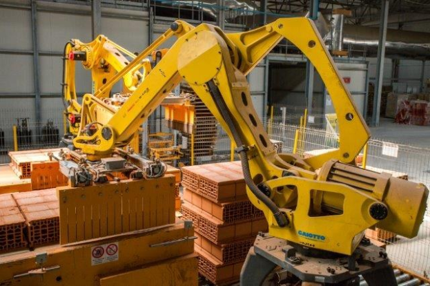 Großes industrielles Lager mit gestapelten Kisten, Kränen an der Decke, Zaun, Pfosten und einer entfernten Wand in einer automatisierten Fertigungsumgebung.