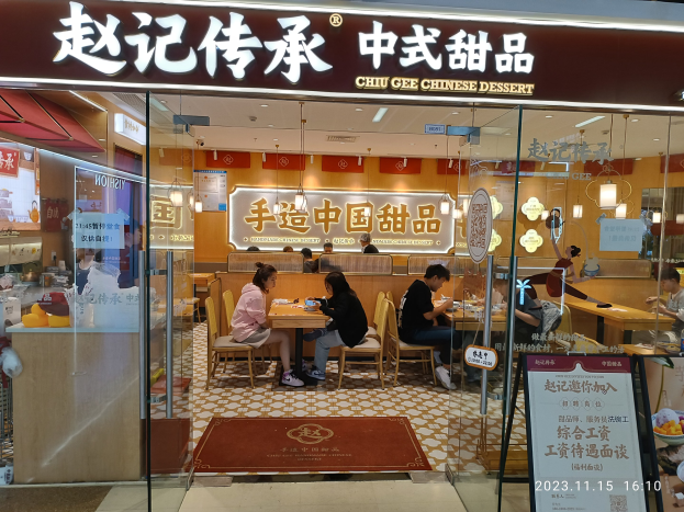 Ein chinesisches Restaurant namens Chiu Gee Chinese Dessert mit Au├čensitzpl├Ątzen, Tischen, Stühlen und einer Glaswand mit Text.