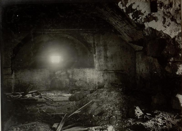 Ein Schwarz-Weiß-Foto eines zerfallenden Tunnels in den Berliner Mauertrümmern, mit Schutt auf dem Boden und einem Licht am Ende.