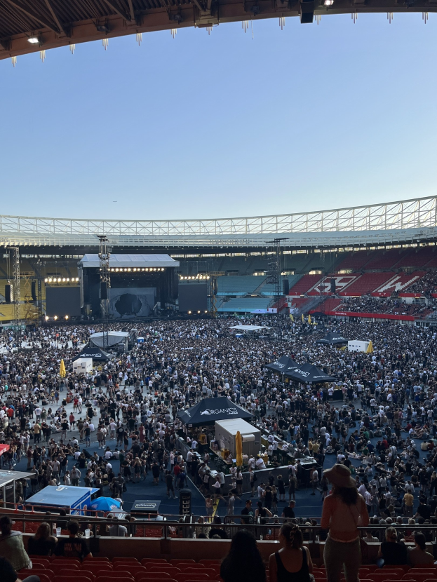 Große Menschenmenge auf Sitzplätzen und Stehplätzen in einer Halle mit Deckenbeleuchtung und Dach, wahrscheinlich in der O2 Arena in London.