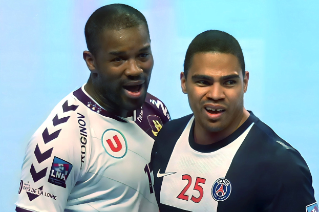 Zwei Männer in weißen und blauen T-Shirts stehen auf einem Fußballfeld und feiern einen Sieg mit einem hellblauen Hintergrund.