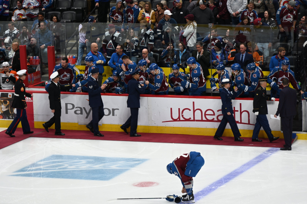Hockeyspieler auf dem Eis umgeben von Teamkollegen und Gegnern, mit Zuschauern und Arena-Beschilderung im Hintergrund.