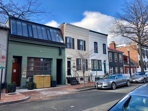 Eine Straße in einem Stadtteil von Philadelphia mit parkenden Autos, Gebäuden, Bäumen, Laternen, Schildern, Holzkisten und einem bewölkten Himmel.