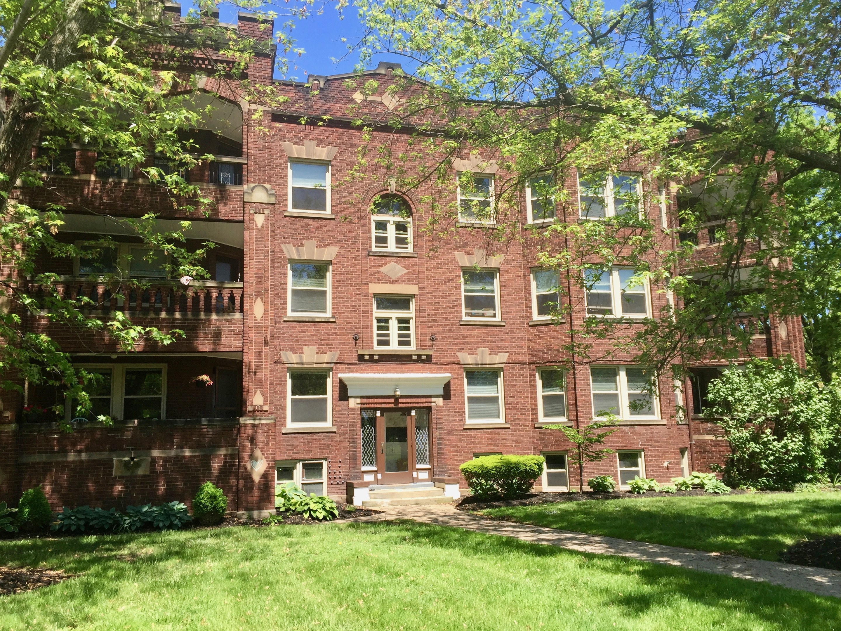 Großes Backsteingebäude mit grünem Rasen, Bäumen und Pflanzen davor, unter einem klaren blauen Himmel, in Chicago, Illinois, zur Miete verfügbar.