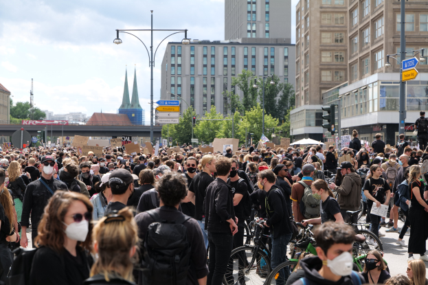 Eine große Gruppe von Menschen mit Masken geht auf einer von Bäumen gesäumten Straße mit Fahrrädern, protestierend in Berlin bei einem bewölktem Himmel.