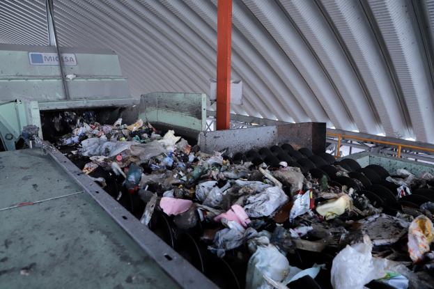 Großer Müllhaufen auf einem Förderband in einer Recyclinganlage mit Maschinen und einem Metalldach