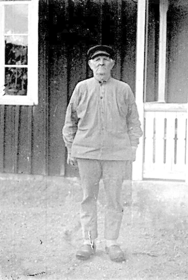 Alter Mann mit Hut vor einem Haus mit Fenster und Tür.