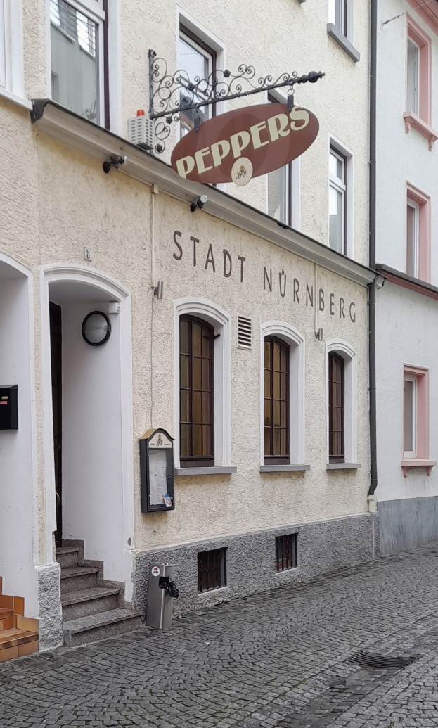 Gebäude mit einer "Stadt Nurnberg"-Aufschrift, Fenstern, einer Tür, einer Treppe und einem Müllcontainer im Vordergrund.