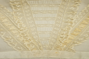 Nahaufnahme eines weißen Kleides mit zarter, kunstvoller Spitzenverzierung auf einem leichten, luftigen Stoff.