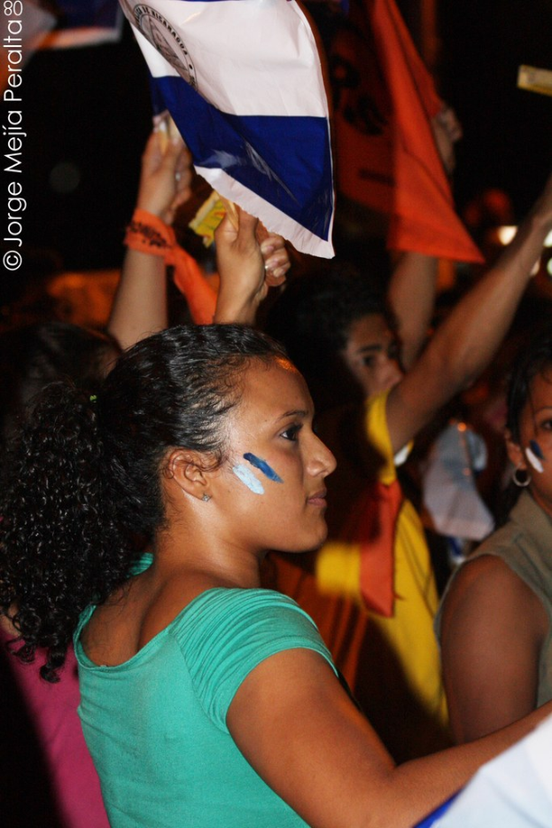 Frauen in grünen T-Shirts mit weißer Hülle, die protestierend mit anderen Mädchen im Hintergrund stehen.