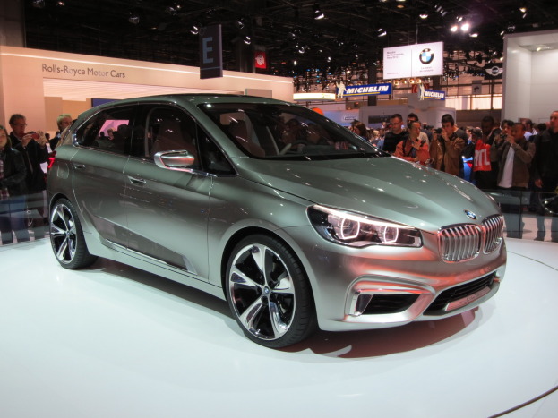 BMW 2er Active Tourer Concept auf der IAA in Frankfurt gezeigt, umgeben von Menschen, die es fotografieren, unter Deckenbeleuchtung mit Informationsschildern im Hintergrund.