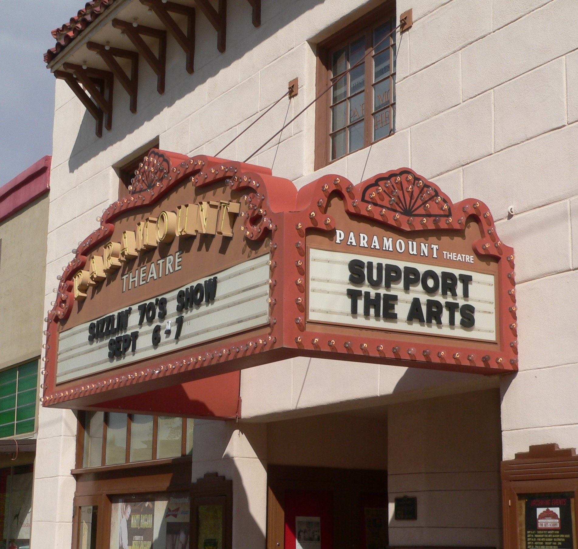 Außenansicht des Paramount Theatre in Sacramento, Kalifornien, mit Glasfenstern und -türen, einem 'Support the Arts'-Schild und einem sichtbaren Himmel im Hintergrund.